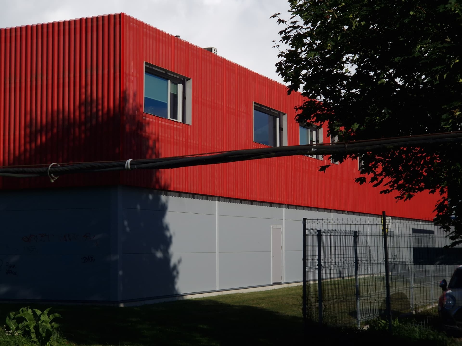 Saue Rimi — red corrugated upper volume with punched windows above the grey plinth
