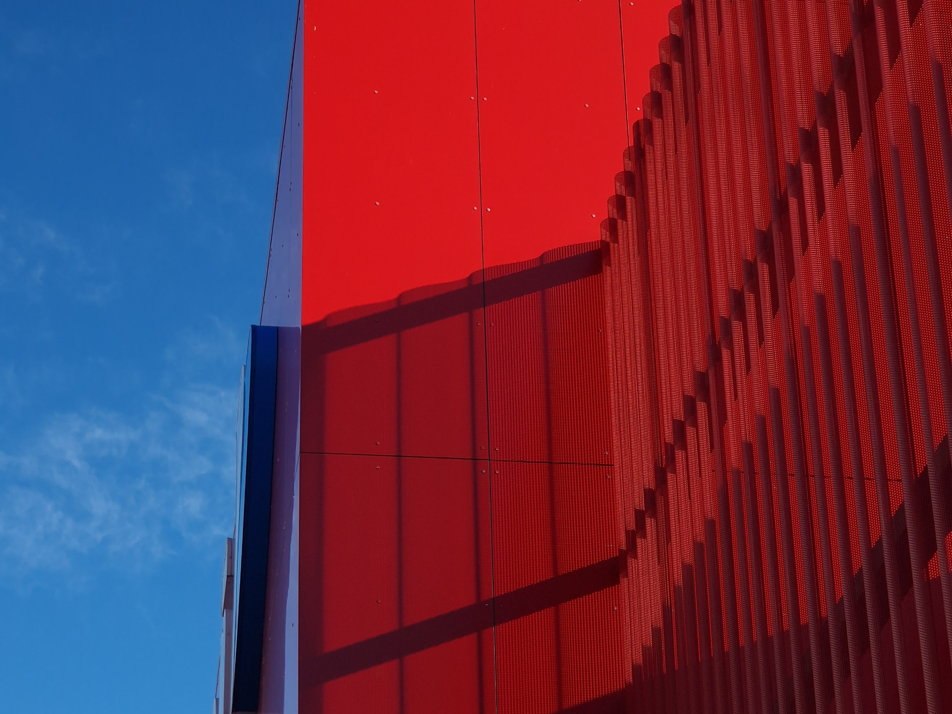 Saue Rimi — facade detail of red panels and perforated metal against the sky
