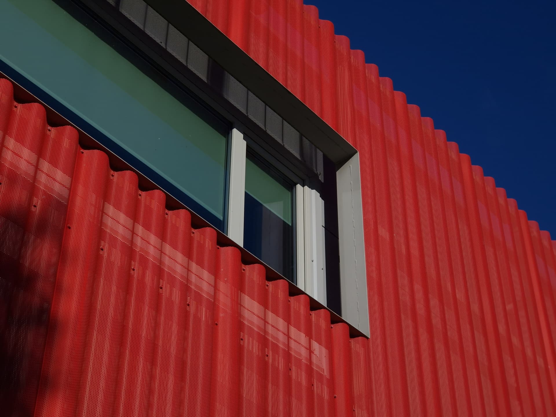 Saue Rimi — perforated red metal facade with a recessed window detail